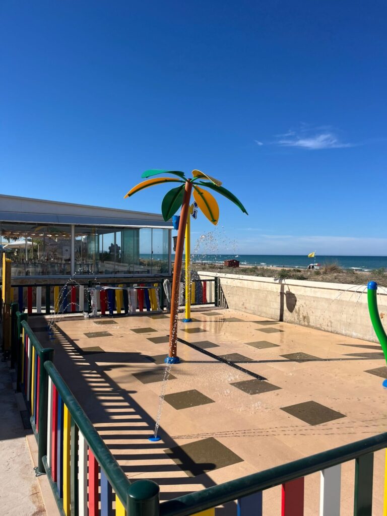 Nice view of the spray park and the sea beach behind, featuring water play floor and equipment!